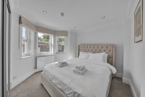 A bedroom with a large bed, a window with a view, and a radiator. - Luxury 3-bedroom Apartment Next to Harrods (London)
