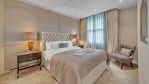 A modern bedroom with a large bed, two bedside tables, a chair, and a large window with curtains. - Elegant Apartment in Marylebone (London)
