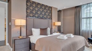 A hotel room with a large bed, two bedside tables with lamps, a decorative wall panel, and a view of the outdoors through the window. - Elegant Apartment in Marylebone (London)