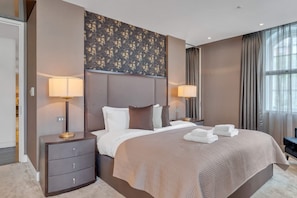 Ein Hotelzimmer mit einem großen Bett, zwei Nachttischen mit Lampen, einer dekorativen Wandverkleidung und Blick ins Freie durch das Fenster.