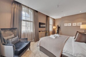 Ein Hotelzimmer mit einem Bett, einem Sessel, einem Schreibtisch, einem Spiegel und einem Fernseher.