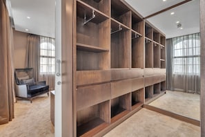 Ein begehbarer Kleiderschrank mit mehreren Regalen und Ablagefläche, ein Sessel und ein großes Fenster mit Vorhängen.