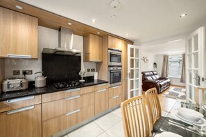 A modern kitchen with wooden cabinets, a gas stove, and an oven. - Three Bedroom Apartment Next to the Station (London)