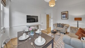 En moderne stue med spiseområde, sofa, tv ophængt på væggen og et mønstret tæppe.