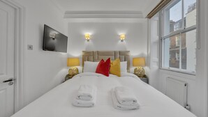 Et hotelværelse med en stor seng, to sengeborde med lamper, et fladskærms-tv og et vindue med udsigt til bygninger.