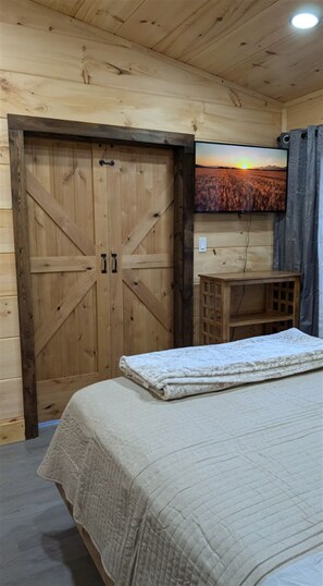 Ein Zimmer mit Holzboden, einem Bett, einem Fernseher an der Wand und einem Holzschrank.