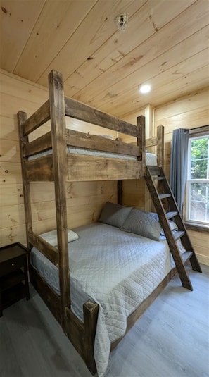 A bunk bed with a wooden frame, a small bedside table, and a window with curtains. - ★ Newly Listed Modern Cabin for Family Adventures and Romantic Escapes ★ (Townsend)