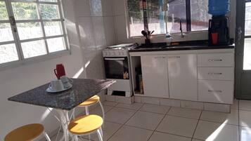 Uma cozinha com fogão, pia e janela. Há banquetas e uma mesa.