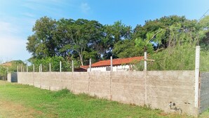 A brick wall with a metal fence, a grassy area, and a building with a red roof.