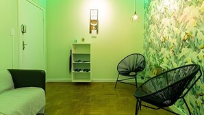 Una habitació amb sòl de fusta, una porta blanca, una estanteria blanca amb sabates, una cadira negra i una paret amb dibuixos florals.
