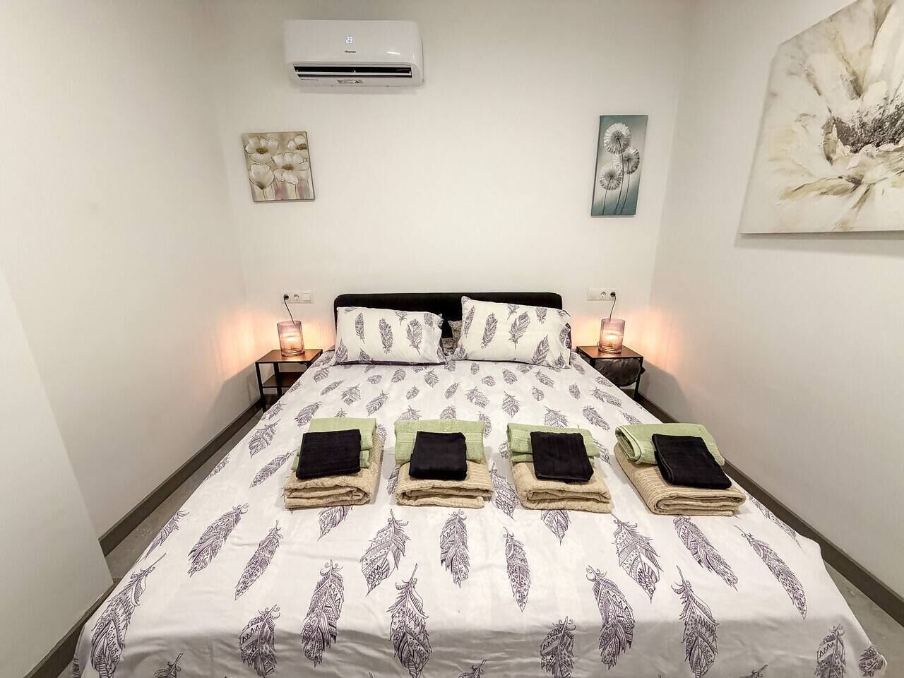 Ein ordentlich gemachtes Bett mit einem gemusterten Bettüberwurf, zwei Nachttische mit Lampen und Wandbildern.