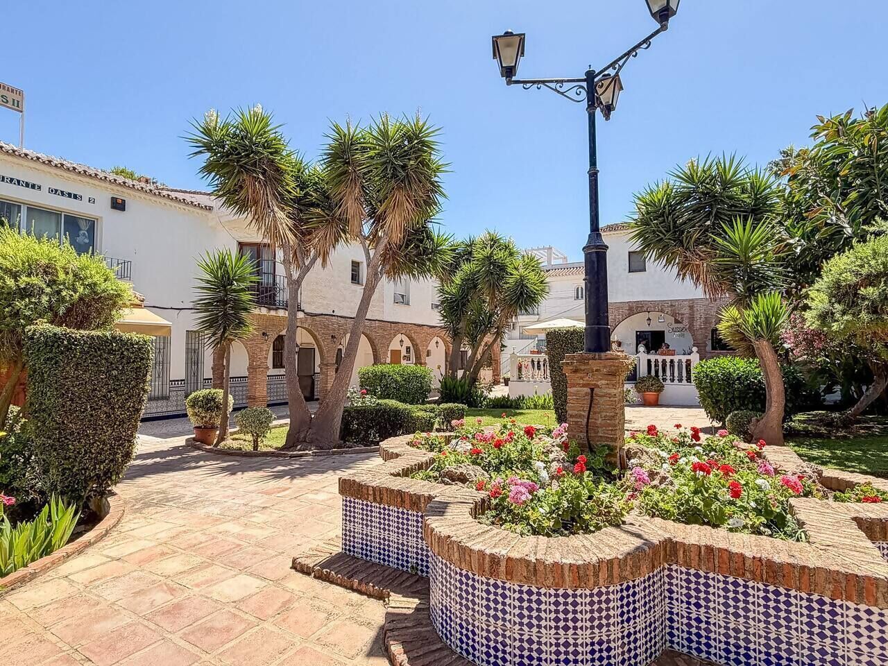Une cour avec un sol carrelé, des palmiers et des parterres de fleurs.