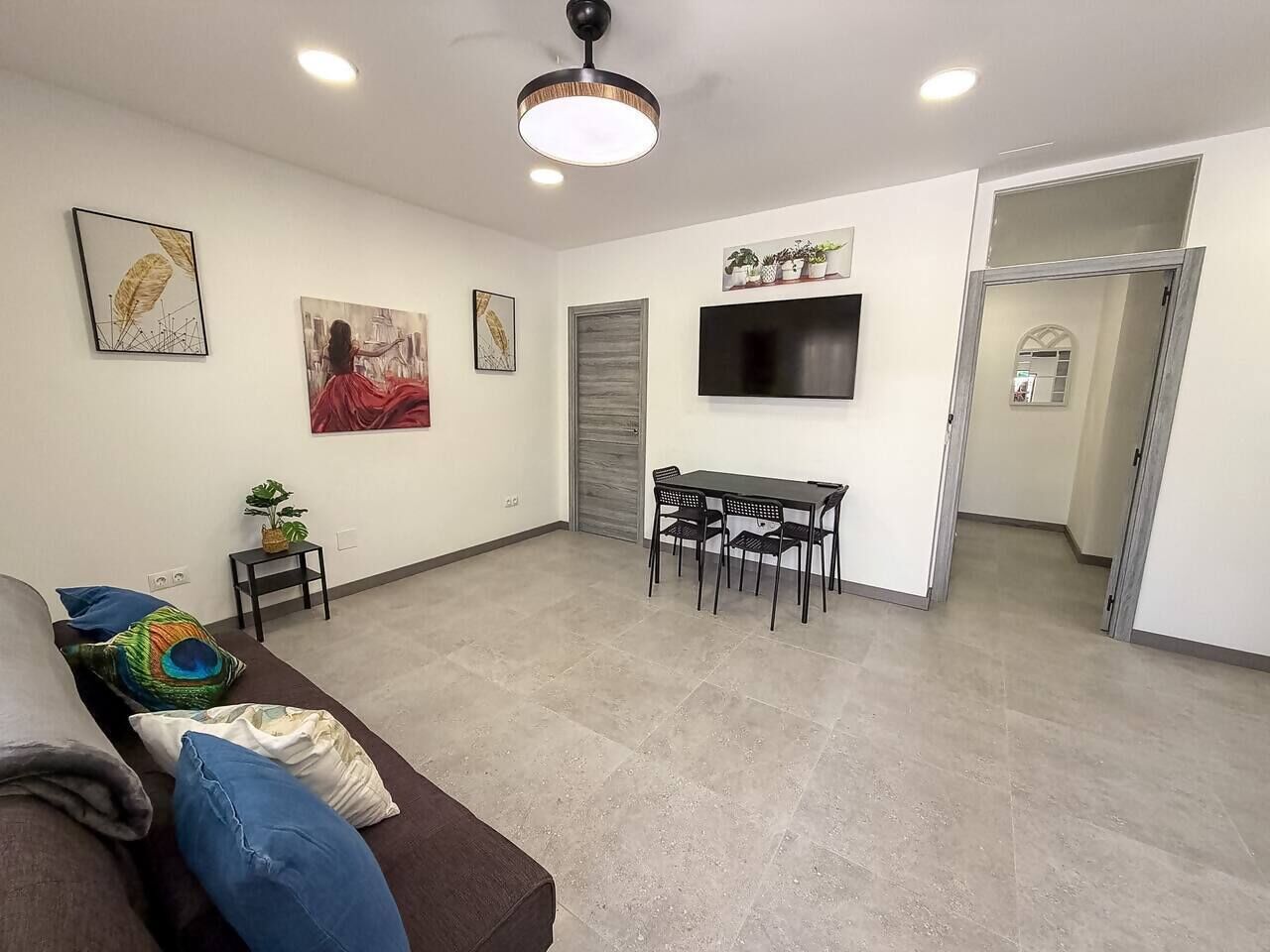 Un salon comprenant un canapé, une table à manger avec des chaises, un téléviseur à écran plat fixé au mur et un ventilateur de plafond.