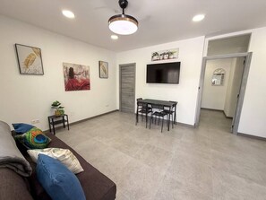 A living room with a sofa, a dining table with chairs, a flat-screen TV mounted on the wall, and a ceiling fan. - Hidden gem! 1 bedroom flat, mins walk to La Cala (Mijas)