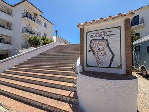 Un escalier menant à un immeuble sur lequel est apposée une plaque indiquant : « Comunidad de Propietarios Pueblo La Cortijera ».