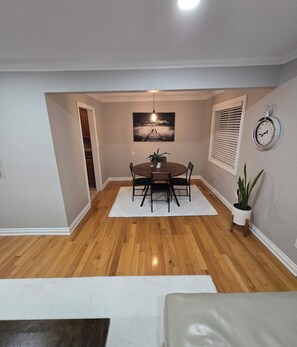 A dining area with a wooden floor, a round table, and chairs. There is a painting above the table and a clock on the wall. - Delightful 2-bedroom apartment with balcony in Sterling Heights (Sterling Heights)