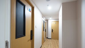 Un pasillo con puertas de madera, piso de color claro e iluminación empotrada en el techo.