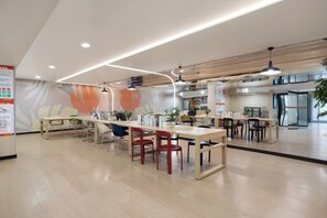 Una biblioteca moderna con mesas y sillas de madera, estanterías y luces de techo.
