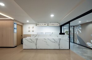 A reception desk with a marble top, wooden paneling on the walls, and a glass door leading to another area. - Xiaobai Youth Hotel (Beijing)