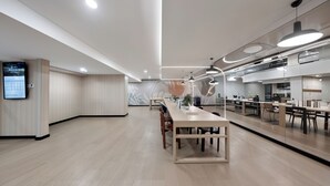 Un interior moderno con una larga mesa de comedor, una zona de cocina y una pantalla digital en la pared.
