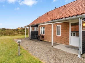A brick building with a tiled roof, a covered patio with a table and chairs, and a gravel driveway. - "Ineke" - 200m from the sea by Interhome (Lemvig)