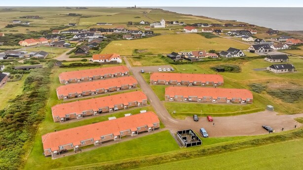 Vista aérea de uma área residencial com várias casas, um farol ao longe e um céu claro.
