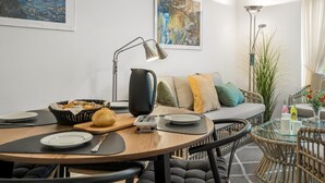 Uma sala de jantar com uma mesa redonda, cadeiras, uma máquina de café e uma cesta de pão.