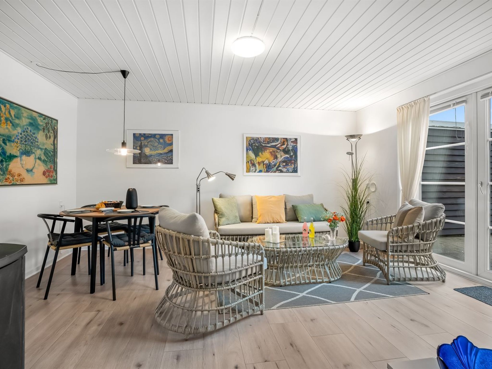 Een moderne woonkamer met een eethoek, rieten meubels en kunstwerken aan de muren.