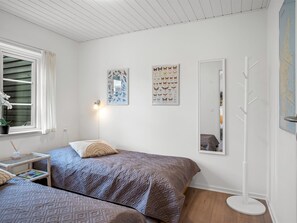 Ein Schlafzimmer mit zwei Betten, einem Nachttisch mit Lampe, einem Fenster mit Vorhängen und Wandbildern.