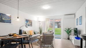 Uma sala moderna com área de jantar, sofá, poltrona de vime e televisão.