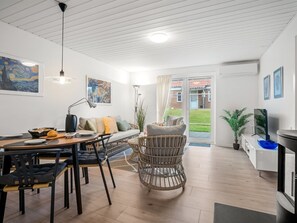 A modern living room with a dining area, a sofa, a wicker chair, and a television. - "Ineke" - 200m from the sea by Interhome (Lemvig)