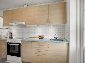 Eine Küche mit Holdekor-Schränken, einer weißen Fliesenrückwand, einer Edelstahl-Spüle und einem eingebauten Backofen.