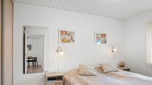 Um quarto com cama, mesas de cabeceira, espelho e quadros nas paredes.