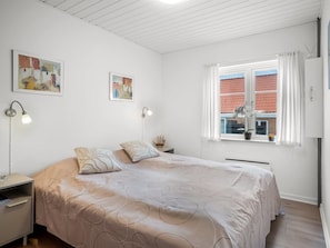 Quarto com cama, duas mesas de cabeceira, janela com cortinas e duas luminárias de parede.