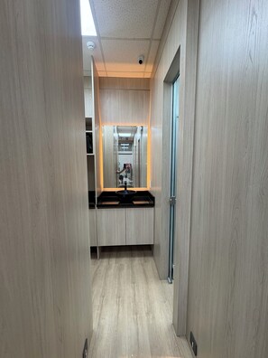 A narrow hallway with wooden walls and a central counter with a sink. - Onkel Inn Airport Sleepbox (Santa Cruz)