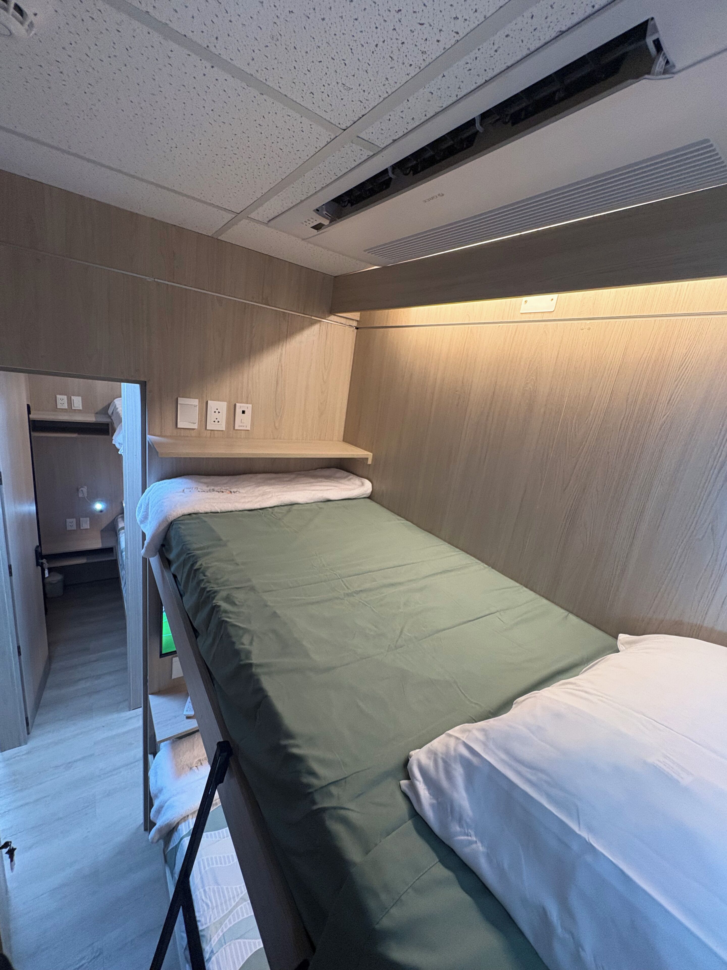 A compact hotel room with a bunk bed, a small closet, and a bedside table.
