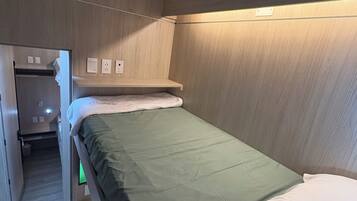 A compact hotel room with a bunk bed, a small closet, and a bedside table.