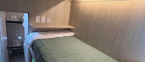 A compact hotel room with a bunk bed, a small closet, and a bedside table.