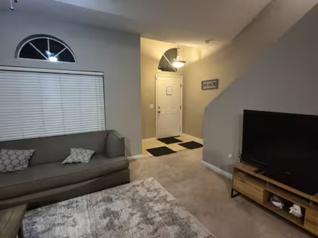 A living room with a sofa, a television, and a carpeted floor.