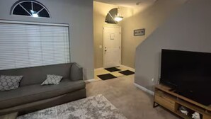 A living room with a sofa, a television, and a carpeted floor. - Minutes to Beach - Cozy Townhouse in PCB (Panama City Beach)