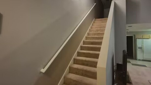 A carpeted staircase with a handrail, a light fixture on the wall, and a partially visible room with a window. - Minutes to Beach - Cozy Townhouse in PCB (Panama City Beach)