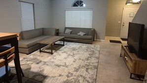 A living room with a sofa, coffee table, TV, and ceiling fan. - Minutes to Beach - Cozy Townhouse in PCB (Panama City Beach)