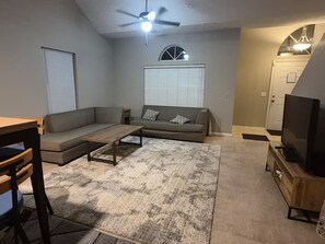 Ein Wohnzimmer mit Sofa, Couchtisch, Fernseher und Deckenventilator.