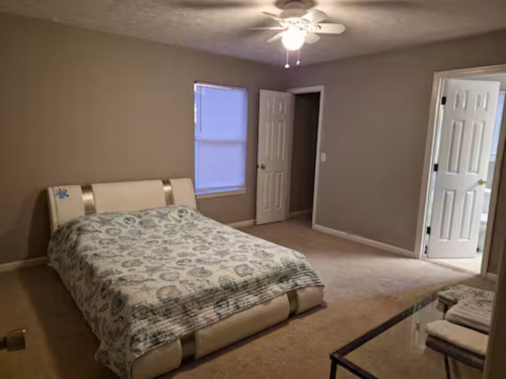 Un dormitorio con una cama, ventilador de techo, ventana y puerta.