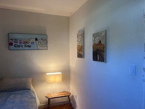 A bedroom with a bed, a bedside table with a lamp, a wall with artwork, and a sign above the bed. - Perfect 3 bedroom house with AC in awesome Petaluma neighborhood near downtown (Petaluma)