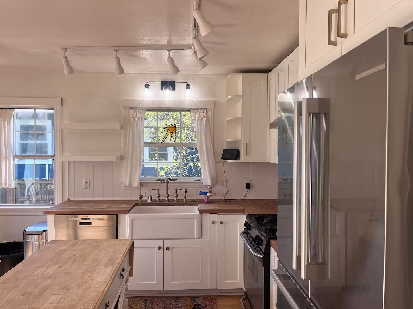 A kitchen with white cabinets, a stainless steel refrigerator, a stove, and a window with a sun design.