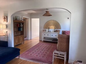 Een kamer met een houten vloer, een blauwe bank, een kamerkleed met dessin, een witte dressoir en een decoratieve spiegel.