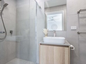 Une salle de bain moderne avec une douche à parois de verre, un lavabo blanc et un ventilateur de plafond.