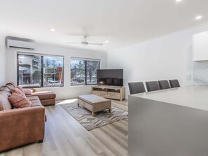 Ein modernes Wohnzimmer mit Sofa, Couchtisch, Fernseher und einem Essbereich mit Stühlen.
