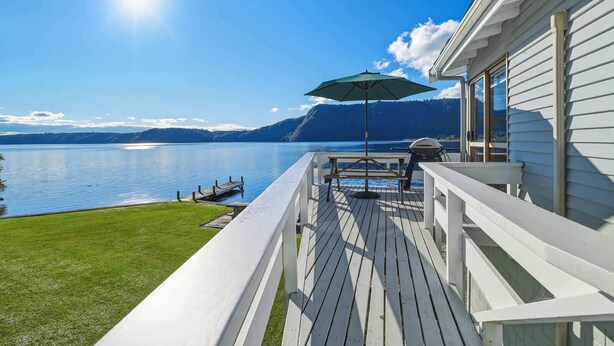 Terraza con una parrilla, una mesa y una sombrilla, con vistas a un lago y montañas al fondo.